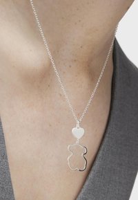 Collar de cadena de plata con un charm de corazón y un colgante con el contorno de un oso. El collar tiene una textura suave y delicados eslabones, llevado sobre la piel desnuda.