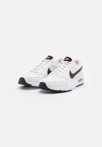 Bijele Nike tenisice s crnim akcentima, teksturiranim mrežastim jezikom, crvenim Nike logom i detaljima zračne amortizacije; gumeni potplat s uzorcima za prianjanje.