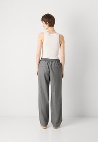 Pantalons larges à rayures grises avec une taille élastique. Le modèle porte un débardeur blanc. Tissu doux avec deux poches arrière.