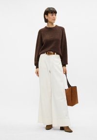 Καφέ πλεκτό πουλόβερ, άσπρα παντελόνια με φαρδιές κατακόρυφες γραμμές, καφέ ζώνη, καφέ μπότες με τετράγωνη φτέρνα και καφέ σουέτ τσάντα tote. Απλός, υφασματικός σχεδιασμός.