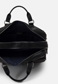 Sac en cuir noir avec deux poignées supérieures et des fermetures éclair en argent. L'intérieur présente un doublure en tissu sombre et un compartiment central pour l'organisation.