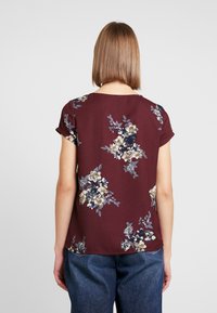 Topy mramorové barvy s květinovým vzorem vyrobené z měkkého materiálu, s krátkými rukávy a kulatým výstřihem, zdobené modrými a krémovými květinovými vzory.