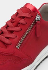 Sneaker rossa in morbido camoscio testurizzato, con lacci piatti, cerniera decorativa laterale e suola in gomma bianca. Presenta un design perforato sulla tomaia.