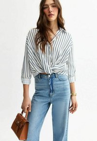 Gestreiftes Hemd in Weiß und Marineblau, am Bund geknotet, kombiniert mit hellblauen High-Waist-Jeans und einer kleinen braunen Handtasche.