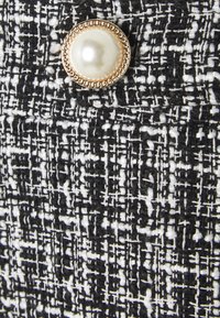 Tissu texturé noir et blanc avec un motif tissé, mettant en avant un bouton rond doré avec un centre ressemblant à une perle.