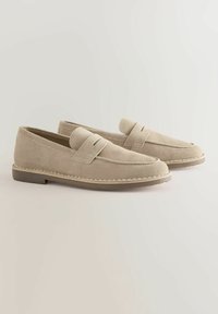 Béžové semišové mokasíny s prošívaným okrajem, plochou podrážkou a páskem přes nárt. Jednoduchý, minimalistický design.