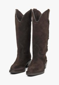 Brązowe zamszowe kozaki do kolan z ostrym noskiem, falbaniastym wykończeniem na górze oraz frędzlami po bokach; z solidnym obcasem i dekoracyjnym szyciem.