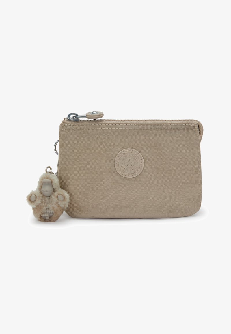 Beige Stofftasche mit Reißverschluss, rundem Logo-Patch und angebrachtem flauschigen Schlüsselanhänger in Form eines kleinen Affen oder Äffchens.