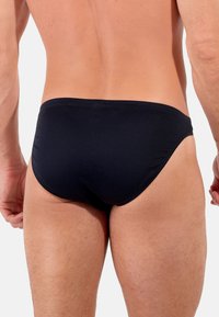 Schwarze Schwimmslips mit glatter Textur, eng anliegendem Design und minimaler Abdeckung, featuring einem weichen elastischen Bund.