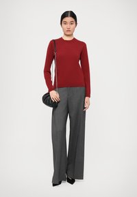 Red long-sleeve sweater paired with gray wide-leg trousers. The model holds a small black handbag with a chain strap.