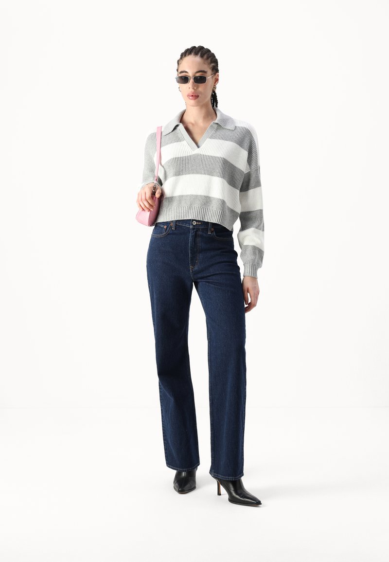 Szary i biały sweter z prążkowanym wzorem, z kołnierzykiem, w połączeniu z ciemnoniebieskimi prostymi spodniami dżinsowymi i czarnymi butami na obcasach z ostrymi noskami. Różowa torebka.