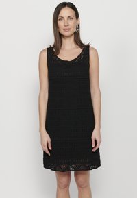 Abito in pizzo nero con design senza maniche, scollatura a barca, motivi testurizzati e vestibilità rilassata. La lunghezza arriva a metà coscia.