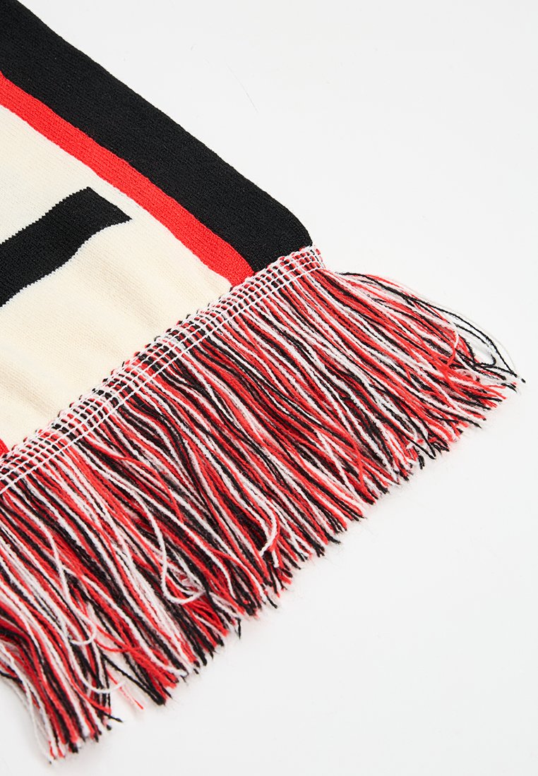 Sweter w formie szala z czarnymi, czerwonymi i kremowymi paskami, o teksturowanym wykończeniu i frędzlami w czerwonych, czarnych i białych włóknach.