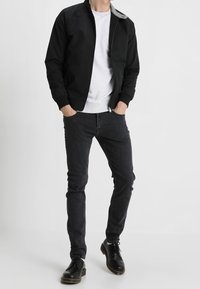 Chaqueta bomber negra con cuello gris, combinada con una camiseta gris, jeans negros ajustados y zapatos negros con cordones. Textura de tela suave en todo.