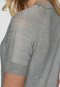 Pull en tricot gris à manches courtes avec un peu de brillance, encolure et poignets côtelés, offrant une coupe décontractée et un léger éclat sur l'ensemble.