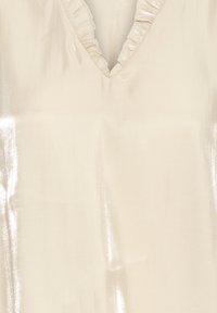Lyse creme top med V-hals og volangkant. Stof har en skinnende, glat tekstur, der reflekterer lys og skaber subtile mønstre.