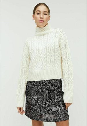 Hvid strikket sweater med høj hals og struktureret mønster, parret med en sort pailetteret nederdel. Begge beklædningsgenstande har en tætsiddende pasform.