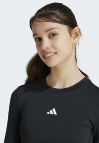 Zwarte lange mouwen sporttop met een ronde hals en een wit logo op de borst. Glad, rekbaar materiaal met een aansluitend ontwerp.