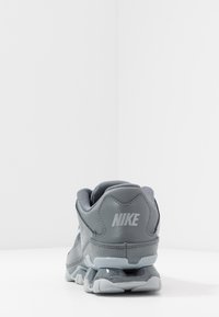 Grauer Nike-Laufschuh von hinten betrachtet, der die gepolsterte Sohle und das Nike-Logo an der Ferse zeigt, vor einem schlichten weißen Hintergrund.