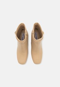 Bottines en cuir beige avec bouts carrés, fermetures éclair latérales et brides à la cheville, vues du dessus sur fond blanc.