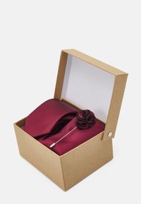 Burgundy solmu, jossa on teksturoitu kuvio, pakattuna pahvilaatikkoon, mukana kangaskukka ja metallipinssi.