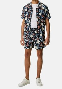 Blommig kortärmad skjorta och matchande shorts i marinblått med vita och rosa blommor. Tillverkad av lättviktig tyg, tillsammans med vita sneakers.