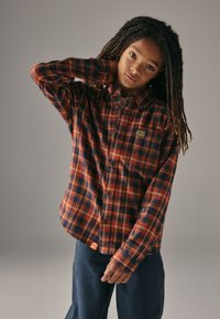 Rød og marineblå ternet flannelsskjorte med knapper, med et lille logopatch. Stoffet virker blødt med en afslappet pasform og lange ærmer.