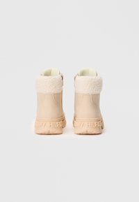Bottines beiges avec doublure en fourrure crème, semelles épaisses embossées du logo "Tommy Hilfiger", vues de l'arrière sur fond blanc.