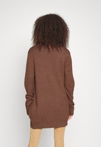 Suéter de punto marrón con mangas largas, un escote redondo y un corte relajado. La textura de la tela parece suave y cálida, con puños y dobladillo acanalados.