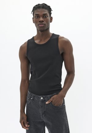 Débardeur noir à côtes avec un col rond et une coupe ajustée, associé à un jean en denim gris foncé avec des détails de bouton et de poche.