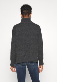 Suéter de punto gris oscuro con un cuello alto y dobladillo acanalado. Presenta un corte holgado y mangas largas, mostrado desde la parte de atrás con jeans azules.