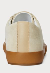 Beige suede sneaker with a smooth leather heel stripe, rubber sole, and textured back. White lining visible at the top opening.