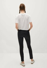 Camiseta blanca de tirantes cortos, jeans negros ajustados, diseño sencillo, tejido suave, combinada con zapatos antideslizantes de color gris claro, vista desde la parte de atrás.