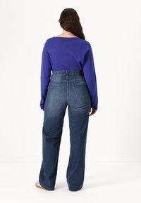Hoch geschnittene, weit geschnittene Jeans aus mittelblauer Denim mit fünf Taschen, kombiniert mit einem langärmeligen, tiefvioletten Pullover.