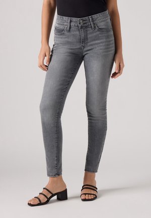 Jean gris taille haute avec une coupe slim, comportant des poches avant et un design épuré. Associé à des sandales à talons blocs noires avec des lanières.