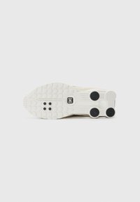 Semelle de chaussure blanche avec des zones de grip circulaires texturées et trois tampons de traction circulaires noirs sur un fond clair uni.