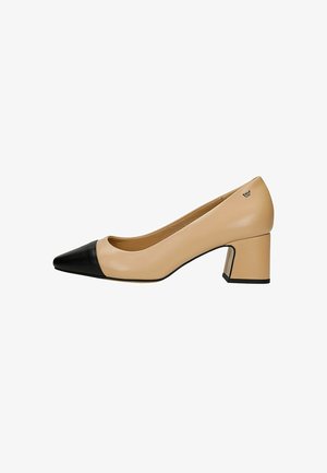 Beige leren pump met lage hak, zwarte puntige neus en blokhak, voorzien van een klein metalen logo bij de hiel.