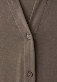 Gros plan sur un cardigan tricoté taupe avec deux boutons ronds et une couture verticale visible le long de l'ouverture en V.