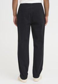 Svarte bomullsbukser med avslappet passform, med to store baklommer og elastisk midjebånd. Enkel, uthulet design, glatt tekstur.