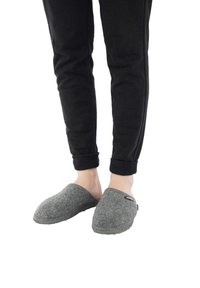 Gray felt slippers with open back, rounded toe, and rubber sole, paired with black tapered pants featuring ribbed cuffs.