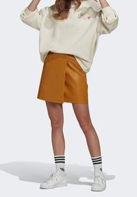 Naturlig läderminikjol med en framfickssöm, ihop med en krämfärgad sweatshirt med blommönsterbroderi, vita sneakers och svartsrandiga strumpor.