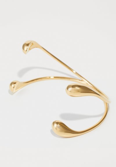Pulsera de muñeca en tono dorado con un diseño curvado y elegante que presenta extremos redondeados y una superficie lisa y reflectante. Estilo ligero y minimalista.
