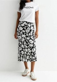 T-shirt bianco con la scritta "Oui Oui", abbinato a una gonna midi nera con motivi floreali bianchi. Indossato con sneakers bianche.