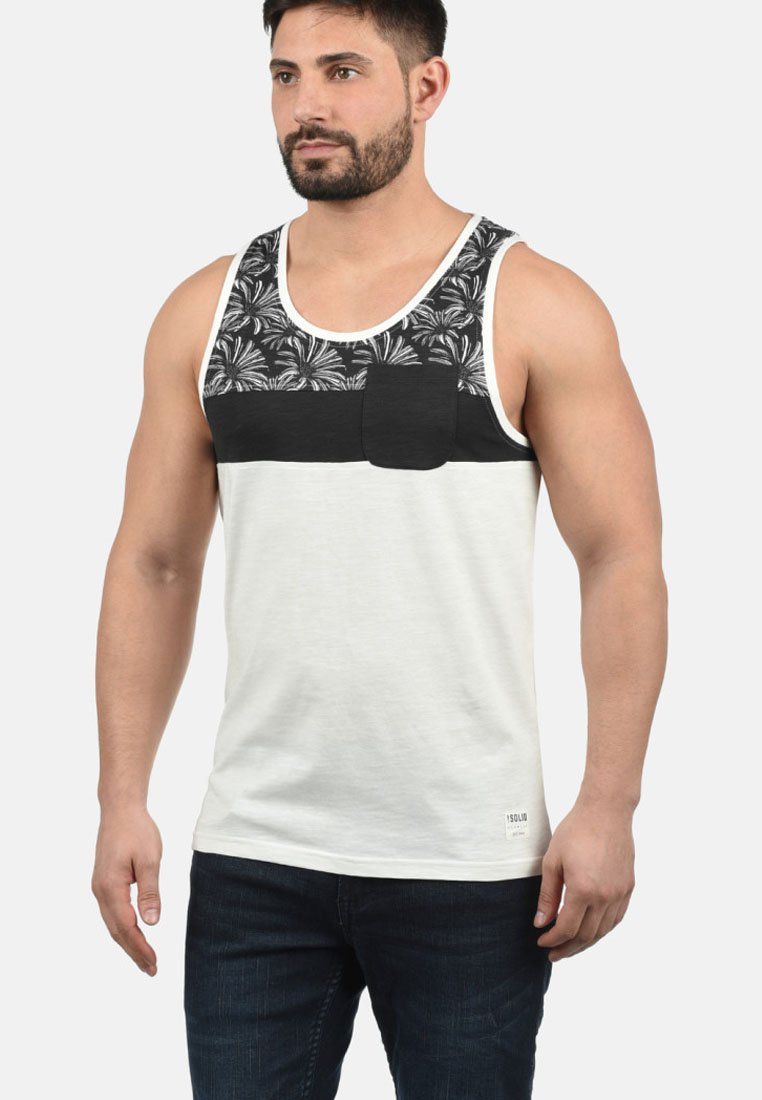 Hvid tanktop med sort mønstret brystpanel, lomme detalje og rund halsudskæring. Serveret med mørke denim jeans.