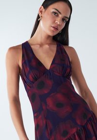 Floral dress in deep purple with large red poppy patterns; features a deep V-neck, gathered bodice, and flowing bottom hem.