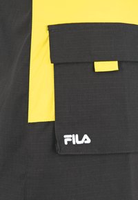 Giacca nera e gialla con un tessuto strutturato, caratterizzata da una grande tasca frontale e logo Fila ricamato in bianco.
