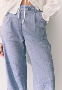 Heledad sinised lina püksid voldidega ja nööpidega vöökohal. Omadusi on pehme tekstuur ja lõdvestunud lõige, sobivad vabaaja kandmiseks.