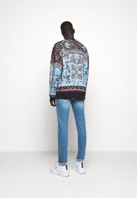 Färgglad mönstrad sweatshirt med blå och svart tyg, med blommönster, som kombineras med ljusblå jeans och vita sneakers.