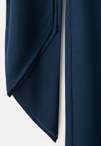 Temno modra tkanina z ostrim trikotnim pregibom in čistimi zašitimi robovi na svetli podlagi.