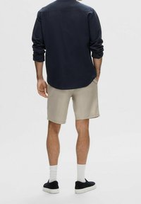 Tenue masculine avec une chemise à manches longues marine, un short beige et des baskets noires avec des chaussettes blanches. Tissu doux, coupe décontractée, design simple.